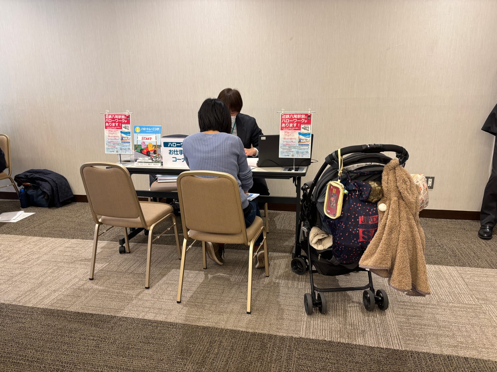 相談ブースで来場者が担当者と話している。そばにベビーカーが置かれている