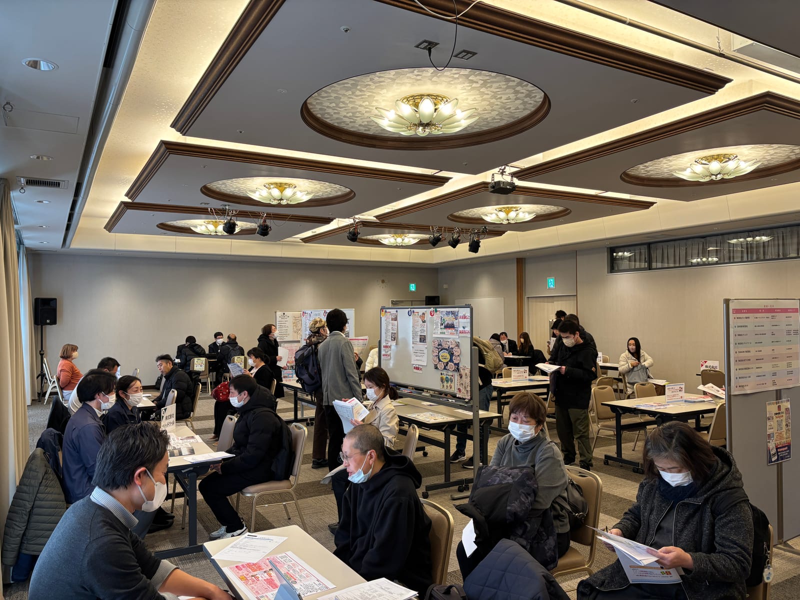 おしごと博の会場全体。シャンデリアのある広間に企業のテーブルが並び、来場者が面談している