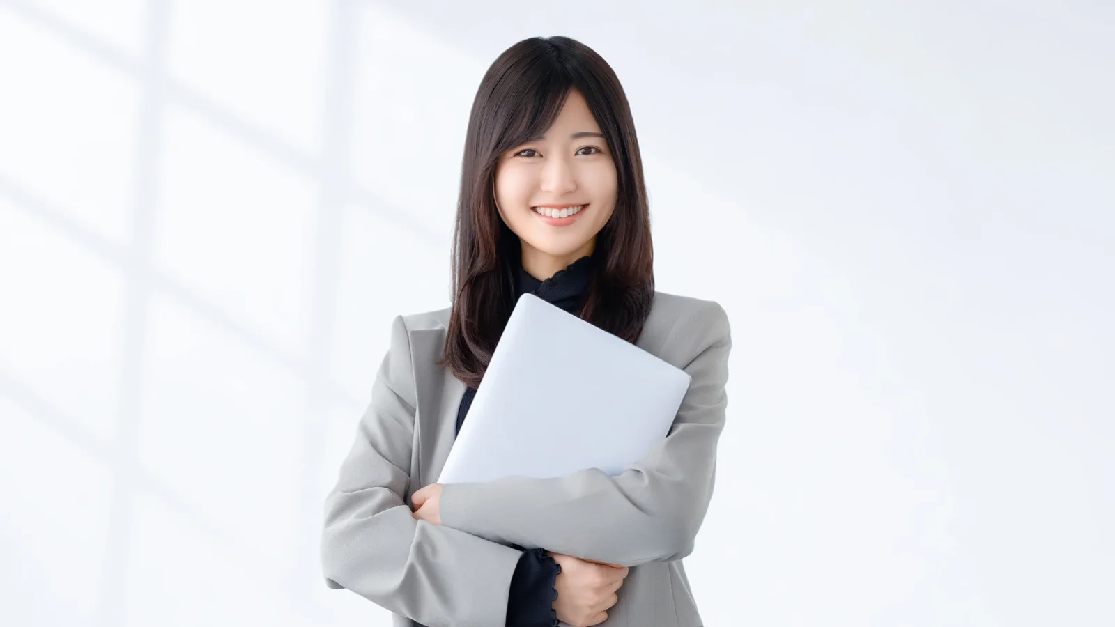 ノートパソコンを抱えて笑顔で立つスーツ姿の女性